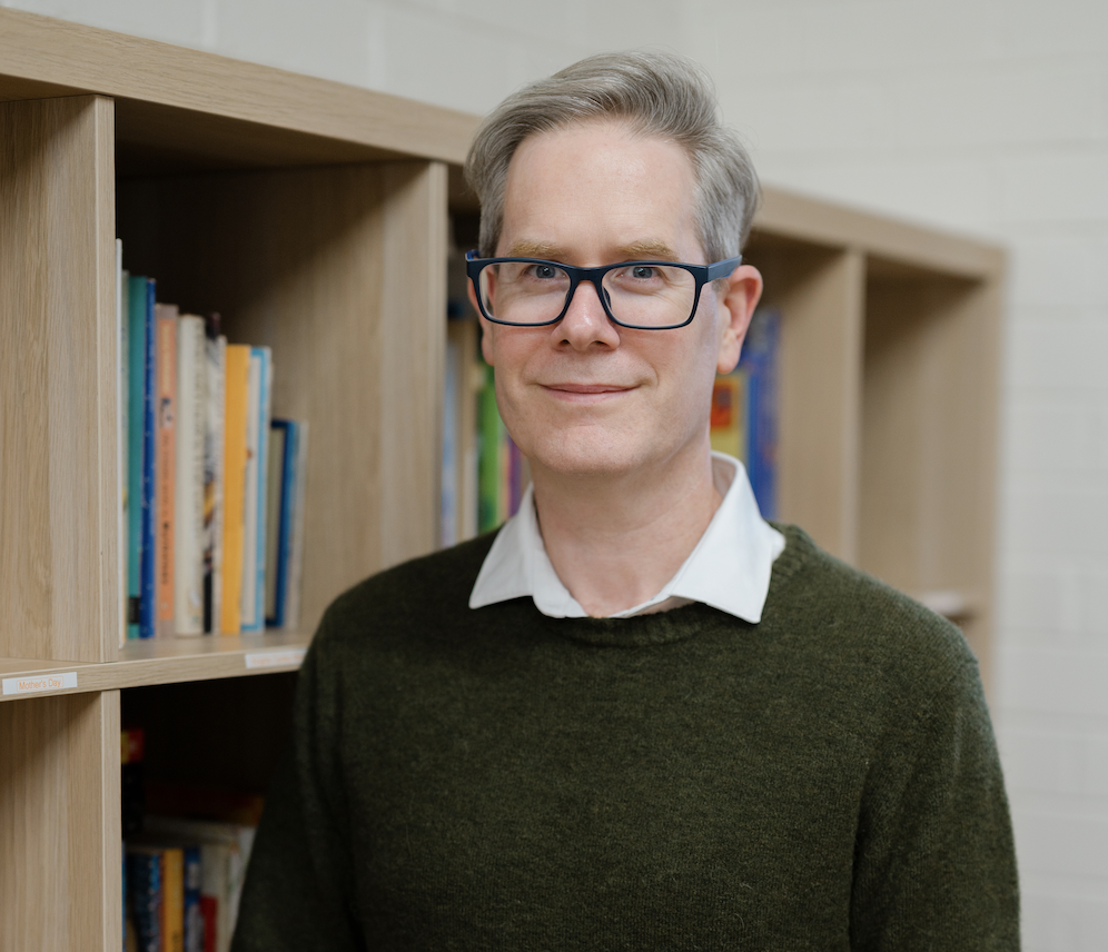 Man with glasses standing in front of a bookcase